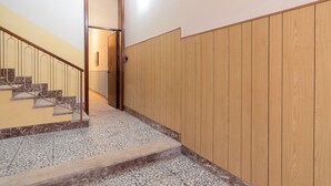 Uma escadaria com corrimão de madeira e piso de azulejo que leva a uma porta.