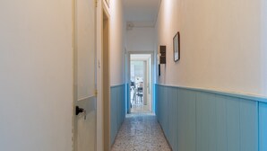 Um corredor com uma porta à esquerda, um quadro na parede direita e piso de azulejos.