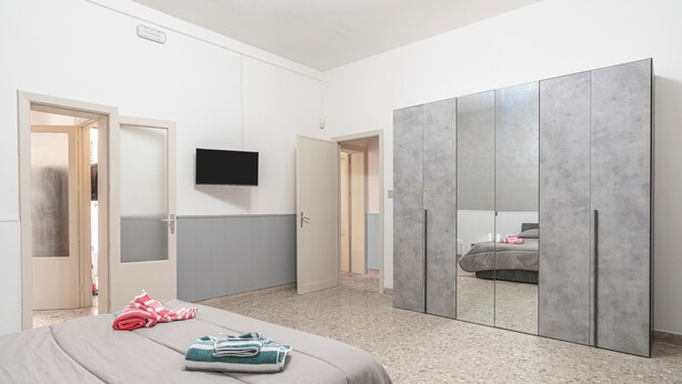 Quarto com cama, televisão, guarda-roupa e porta que dá para outro cômodo.