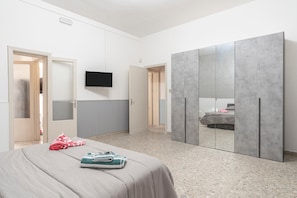 A bedroom with a bed, a TV, a wardrobe, and a door leading to another room.