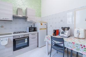 A compact kitchen with a gas stove, microwave, oven, refrigerator, and a table with a floral tablecloth.
