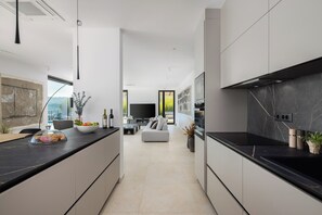 A modern kitchen with a black countertop, white cabinetry, and a large island. There is a dining area with a sofa and a TV in the background. - Incredible divine view 5-bedroom villa in Vis Town (Vis)