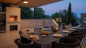 An outdoor dining area with a stone wall, a built-in fireplace, wicker chairs, and a table set for a meal. - Incredible divine view 5-bedroom villa in Vis Town (Vis)