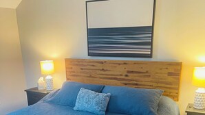 A bedroom with a large bed, wooden headboard, two bedside tables with lamps, and a framed picture above the bed. - Spacious 4BR Retreat Near Downtown Elk Rapids. Walk to Shops, Dining & the Bay (Elk Rapids)