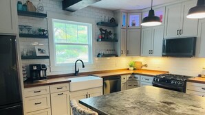 A modern kitchen with white cabinetry, a large island, a built-in stove, and a window providing natural light. - Spacious 4BR Retreat Near Downtown Elk Rapids. Walk to Shops, Dining & the Bay (Elk Rapids)