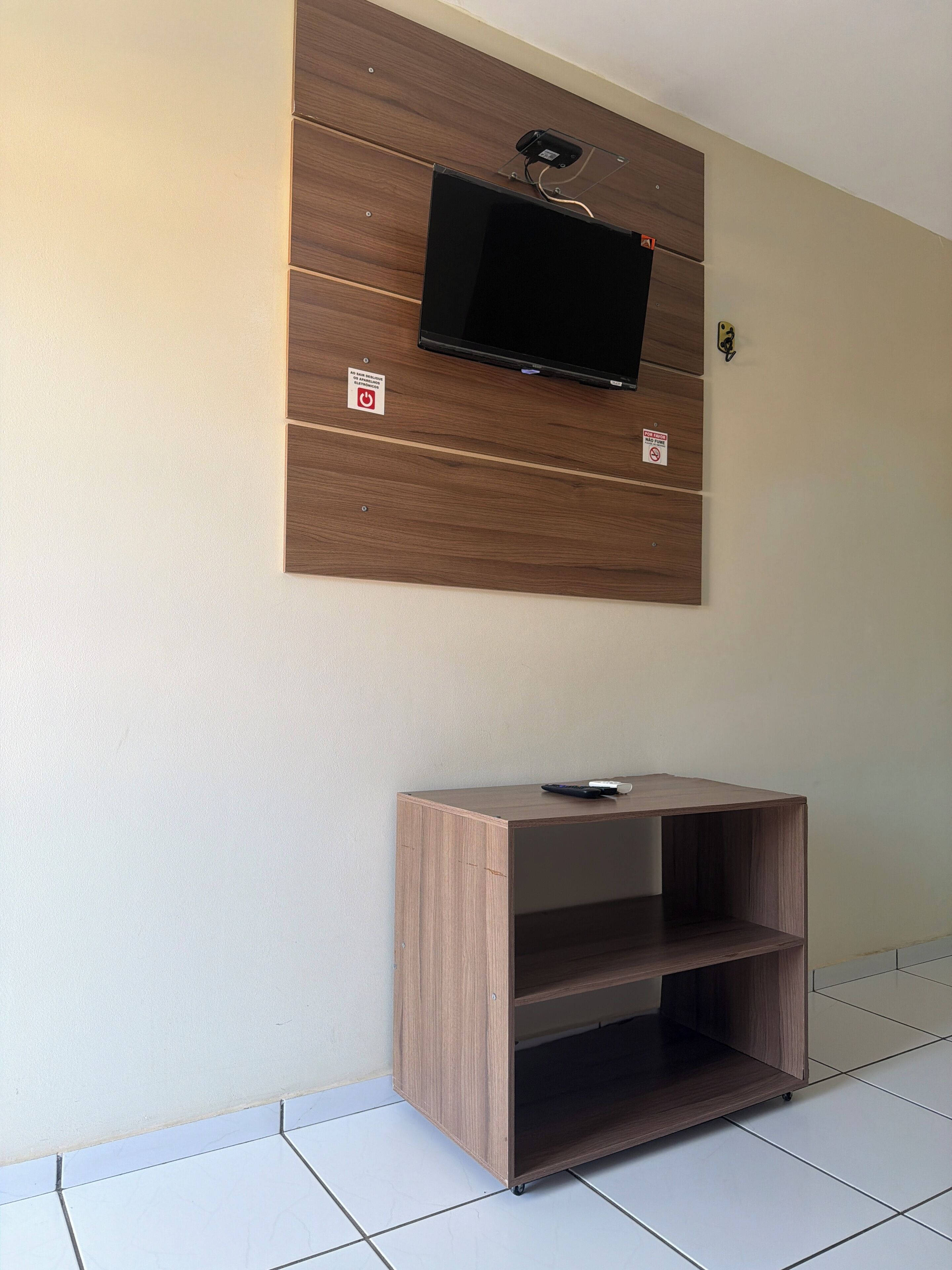 Een aan de muur bevestigde televisie op een houten paneel, met een klein plankje eronder.
