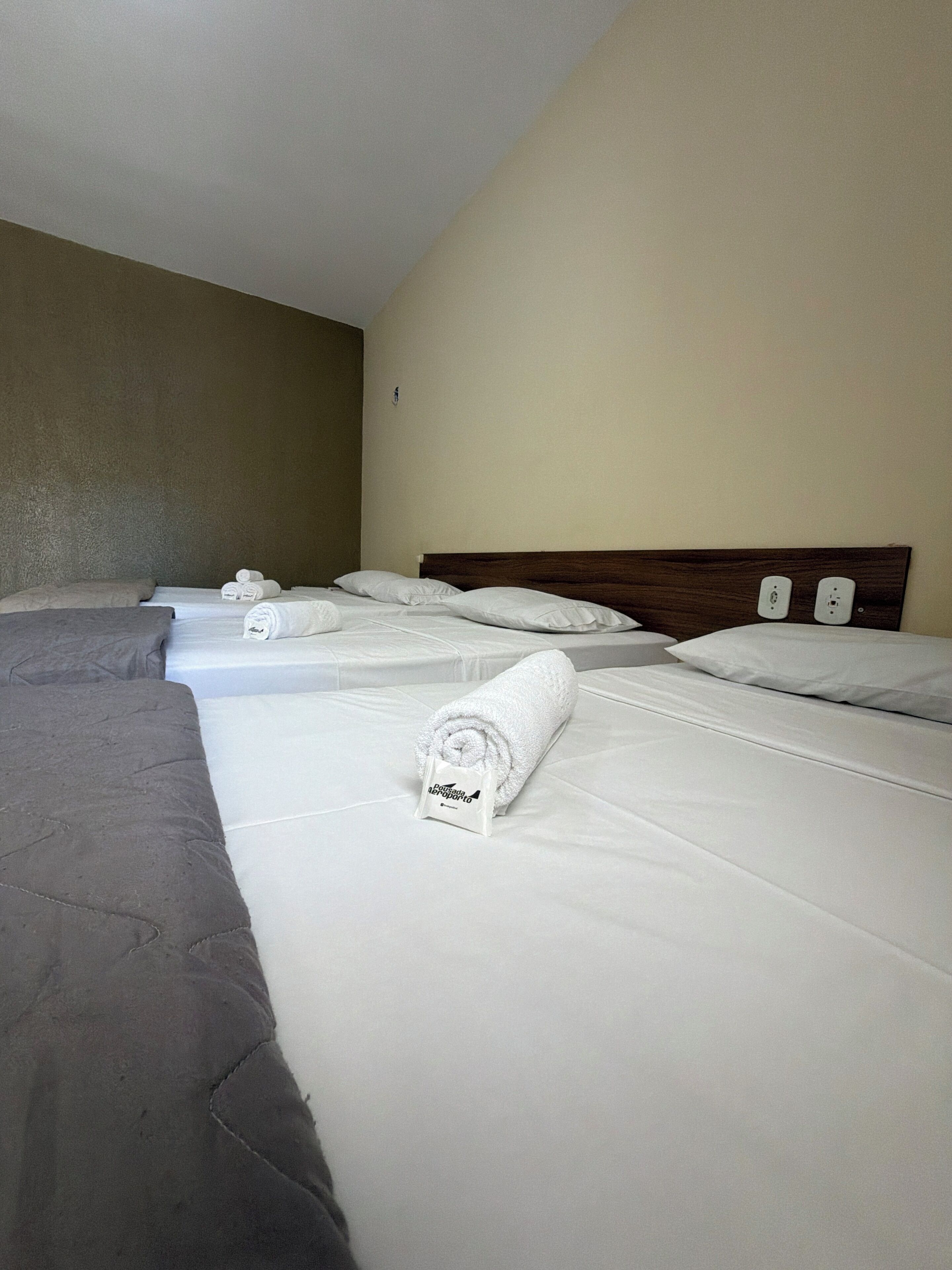 Habitación de hotel con dos camas, cada una con toallas blancas ordenadas y un cabecero de madera.