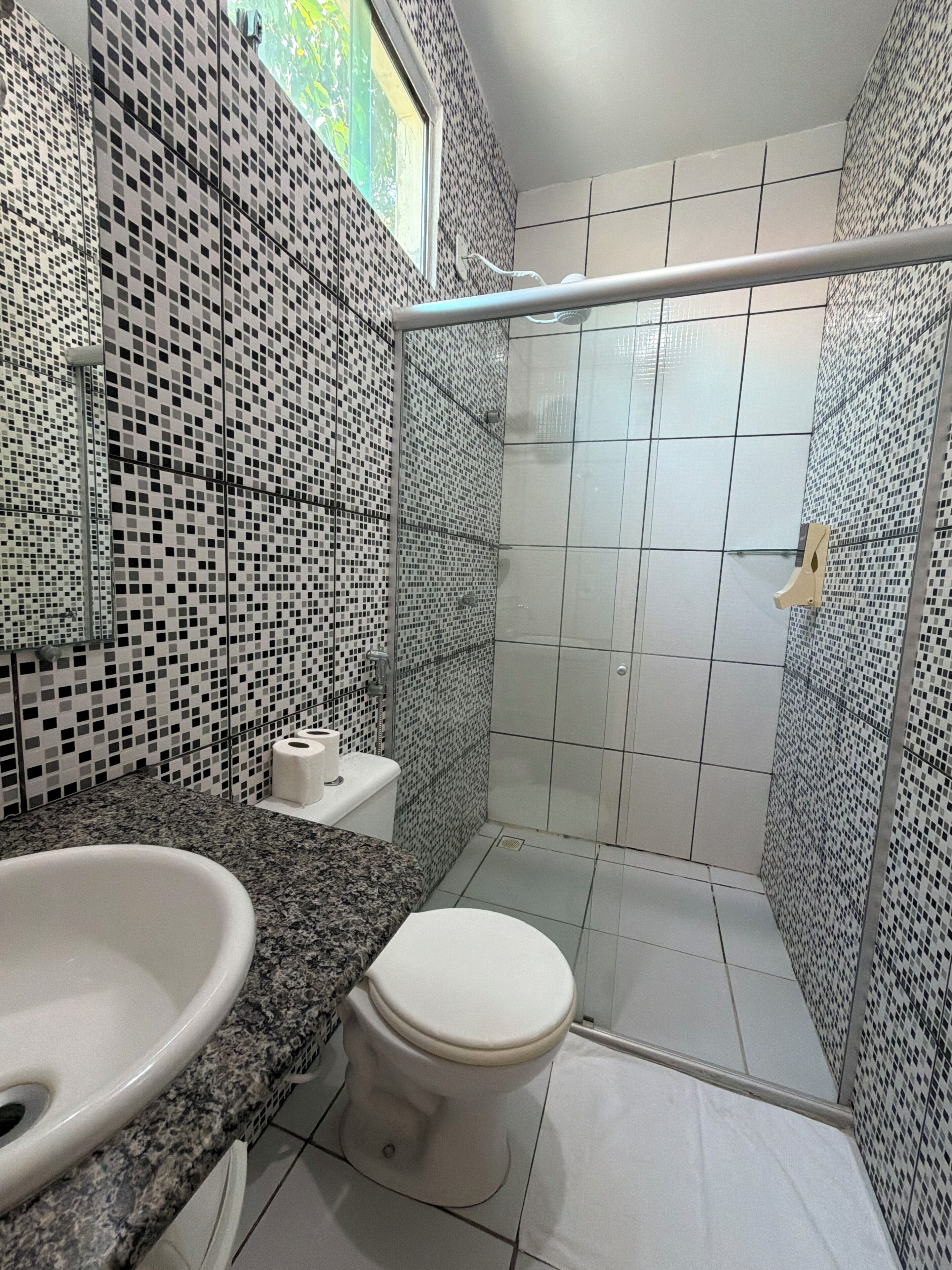 A bathroom with a mosaic tile wall, a white toilet, a granite countertop, and a shower area.