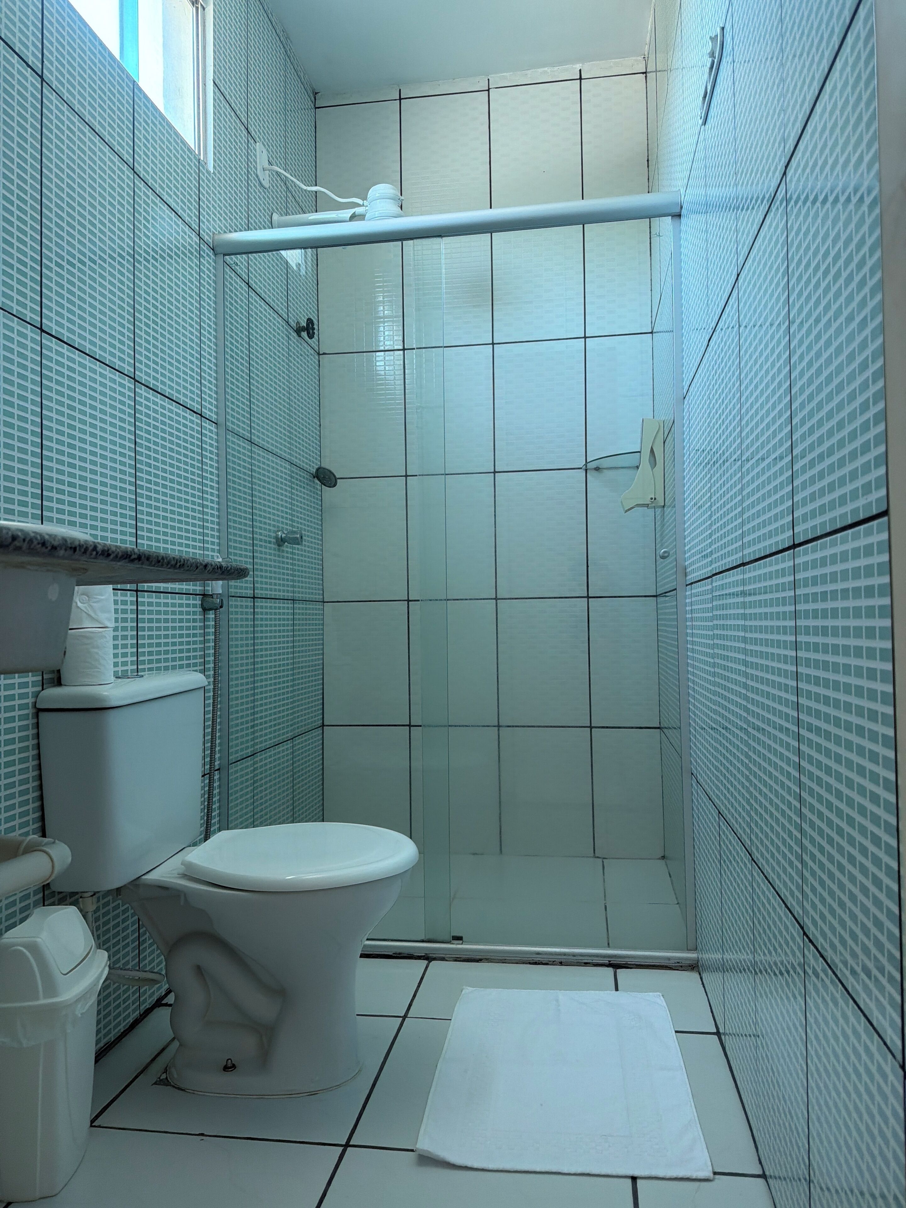 A small, tiled bathroom with a toilet, a shower, and a towel on the floor.