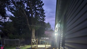 A backyard with a paved pathway leading to a fenced area, a wooden deck, and a house with a metal siding exterior. - Forest City (room for one person) #3 (London)