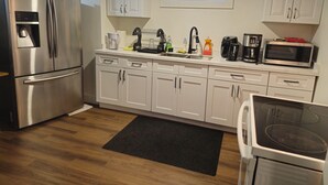 A modern kitchen with white cabinets, stainless steel appliances, and a black mat on the floor. - Forest City (room for one person) #3 (London)