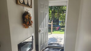 A hallway with a dark carpet leading to a door, a wall-mounted decorative item, and a view of a playground outside. - Forest City (room for one person) #3 (London)