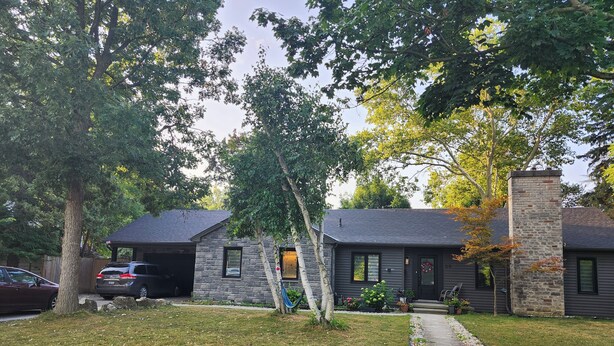 A two-story house with a stone chimney, a garage, and a well-maintained lawn. - Forest City (room for one person) #3 (London)