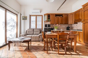Una cocina con armarios de madera, una mesa de comedor con sillas, un sofá y un amplio ventanal con cortinas.