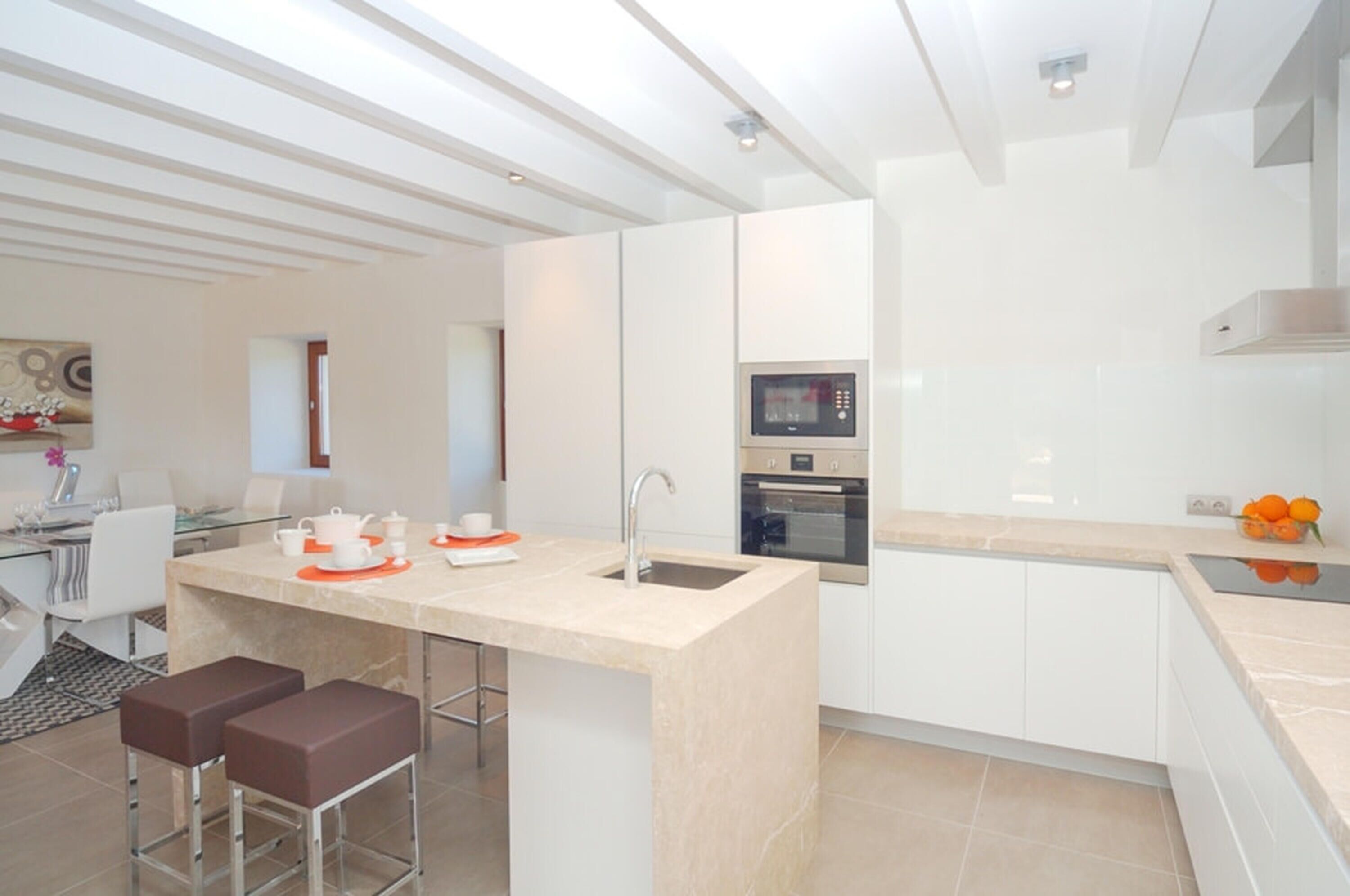 A modern kitchen with white cabinetry, a central island with stools, a built-in oven, and a microwave.
