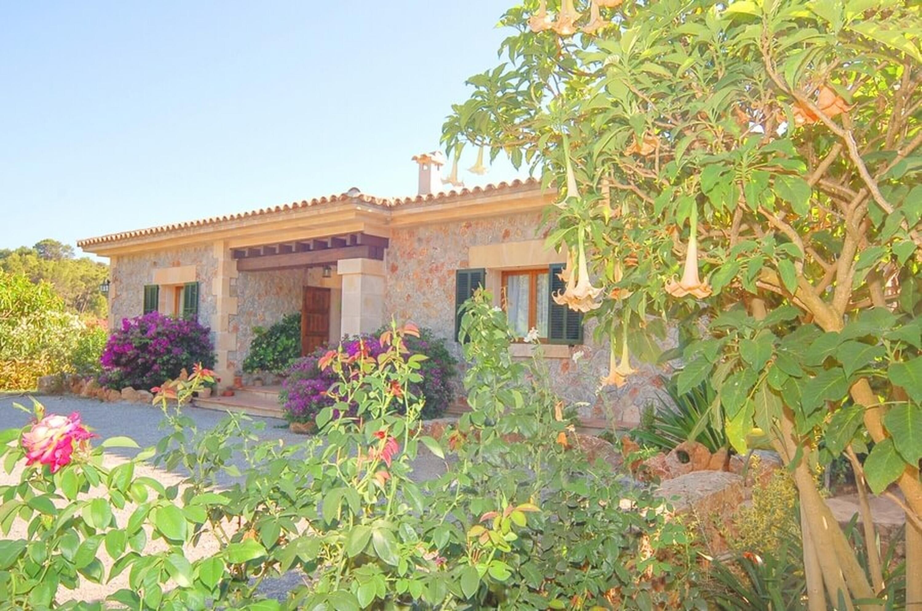 A stone house with a tiled roof, surrounded by lush greenery and flowering plants.