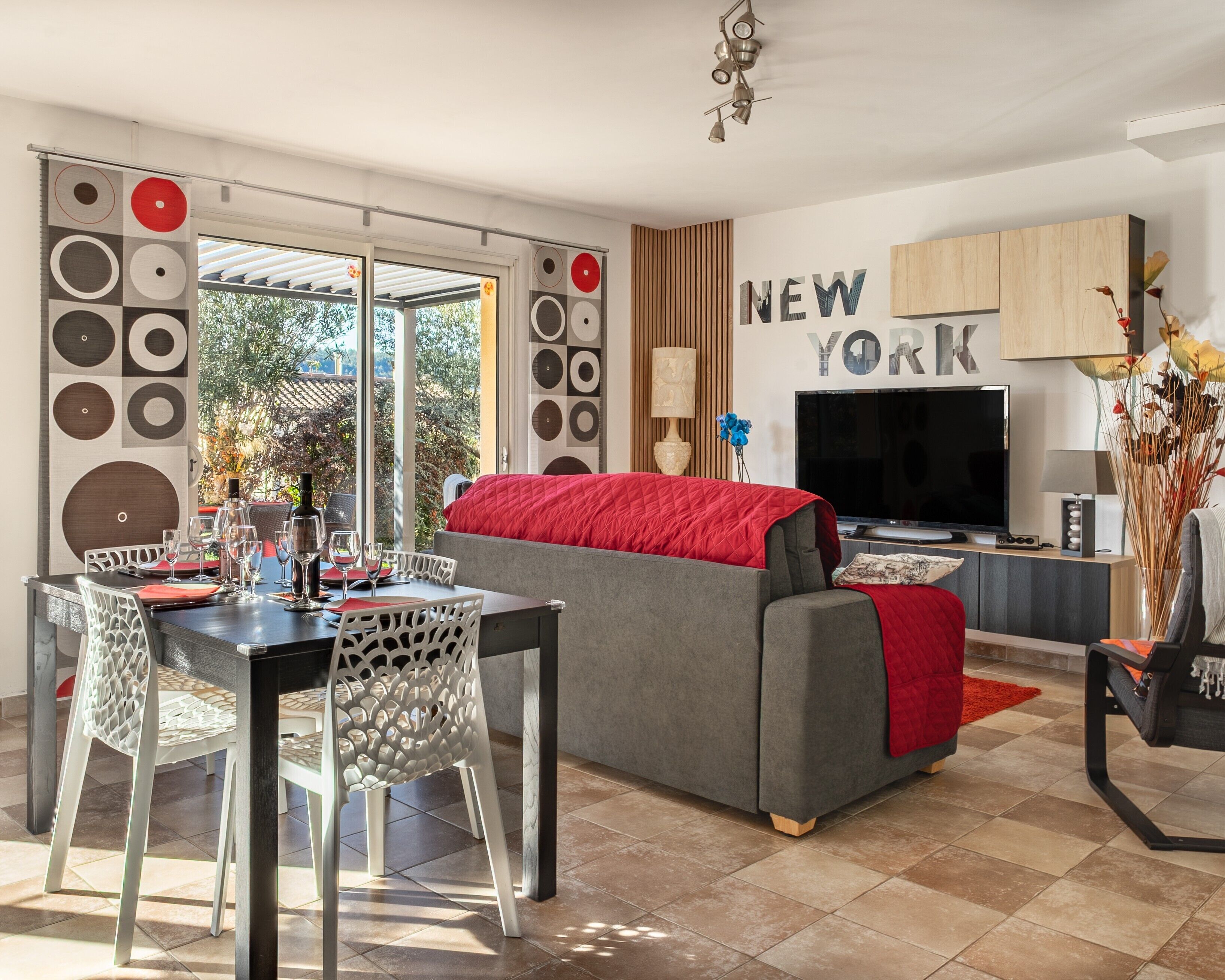 Una sala de estar moderna con un sofá gris, una mesa de comedor con sillas, un televisor y una pared con el texto 'NEW YORK'.