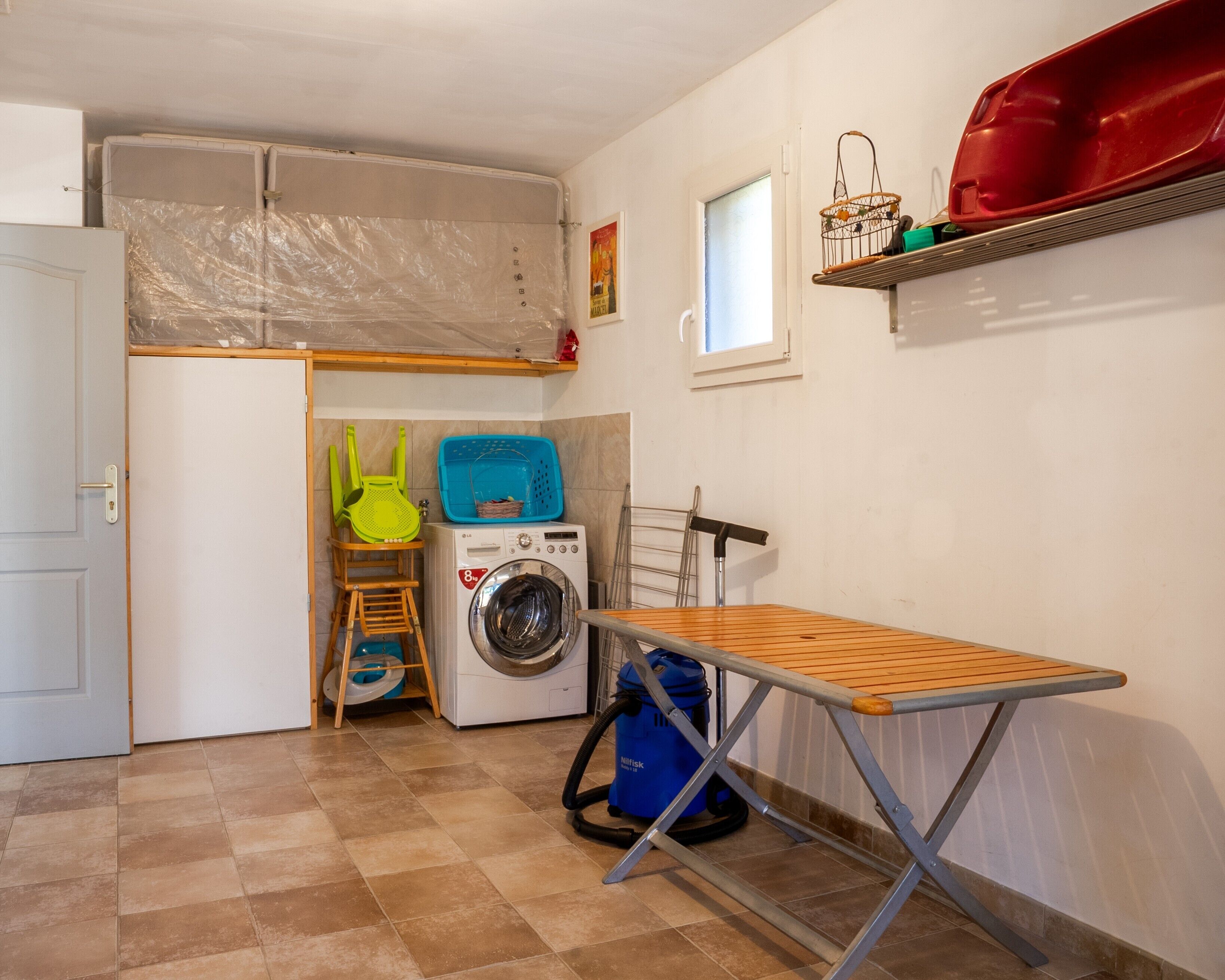 A laundry room with a washing machine, drying rack, and a small window.