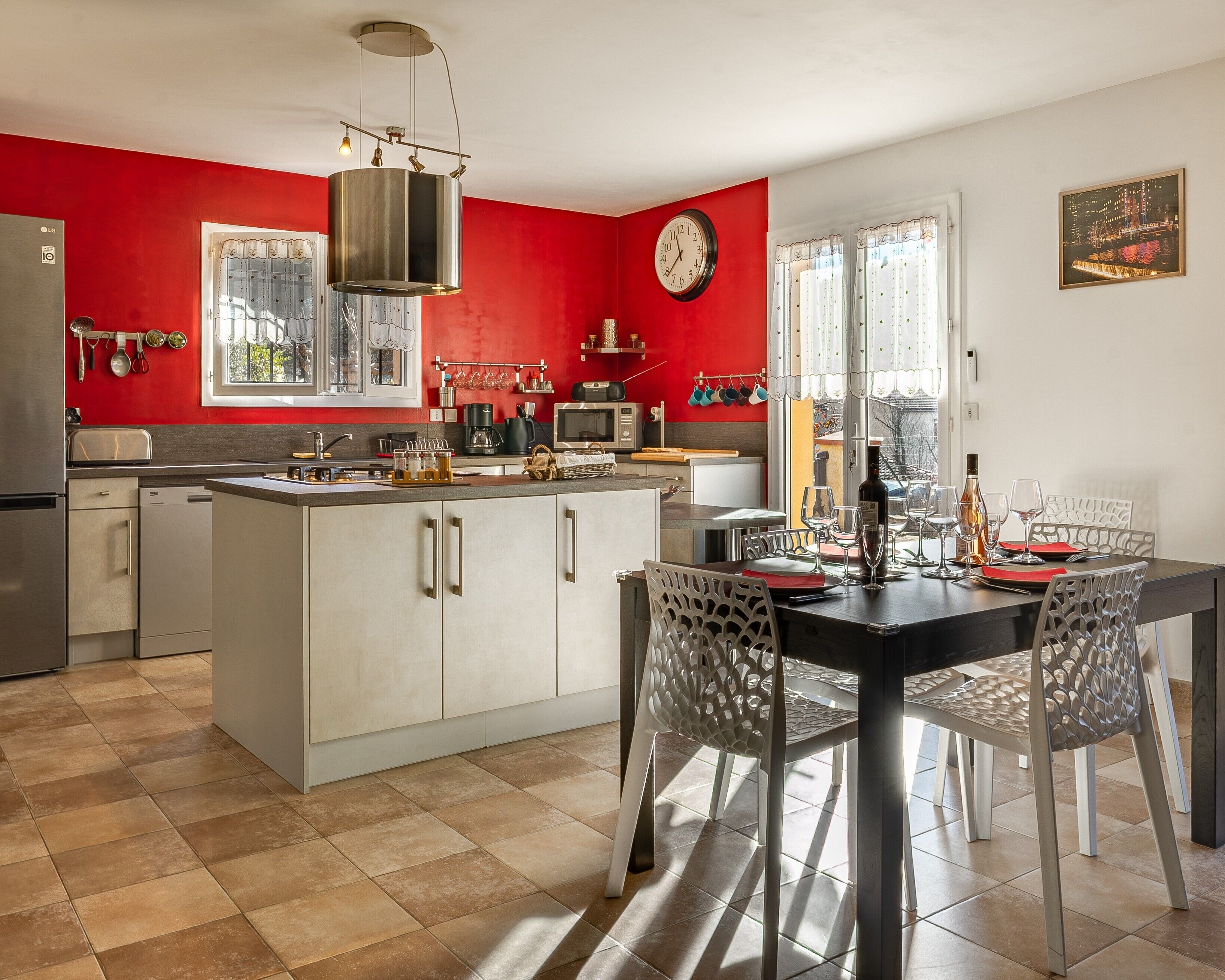 Une cuisine moderne avec un mur d’accent rouge, un coin repas avec une table et des chaises, et une horloge au mur.