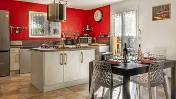Une cuisine moderne avec un mur d’accent rouge, un coin repas avec une table et des chaises, et une horloge au mur.
