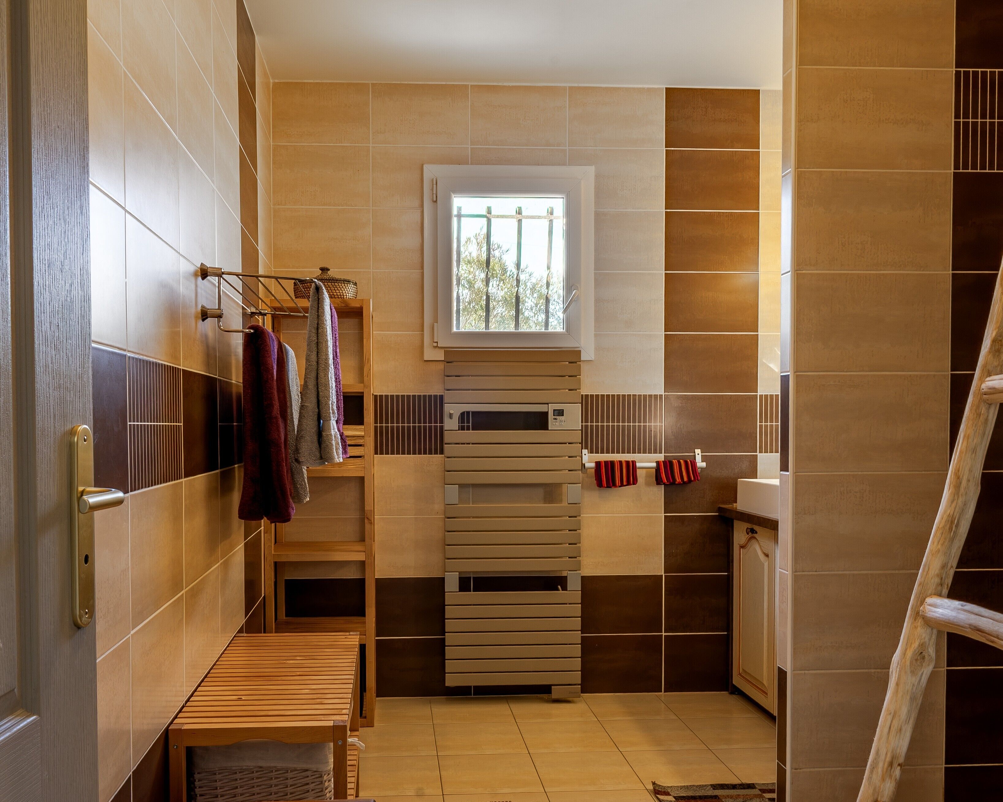 Une salle de bain avec un banc en bois, un porte-serviettes et une fenêtre.