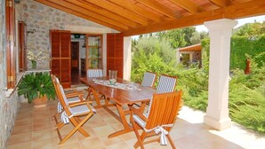 Un patio al aire libre con mesa y sillas de madera, rodeado de muros de piedra y follaje.