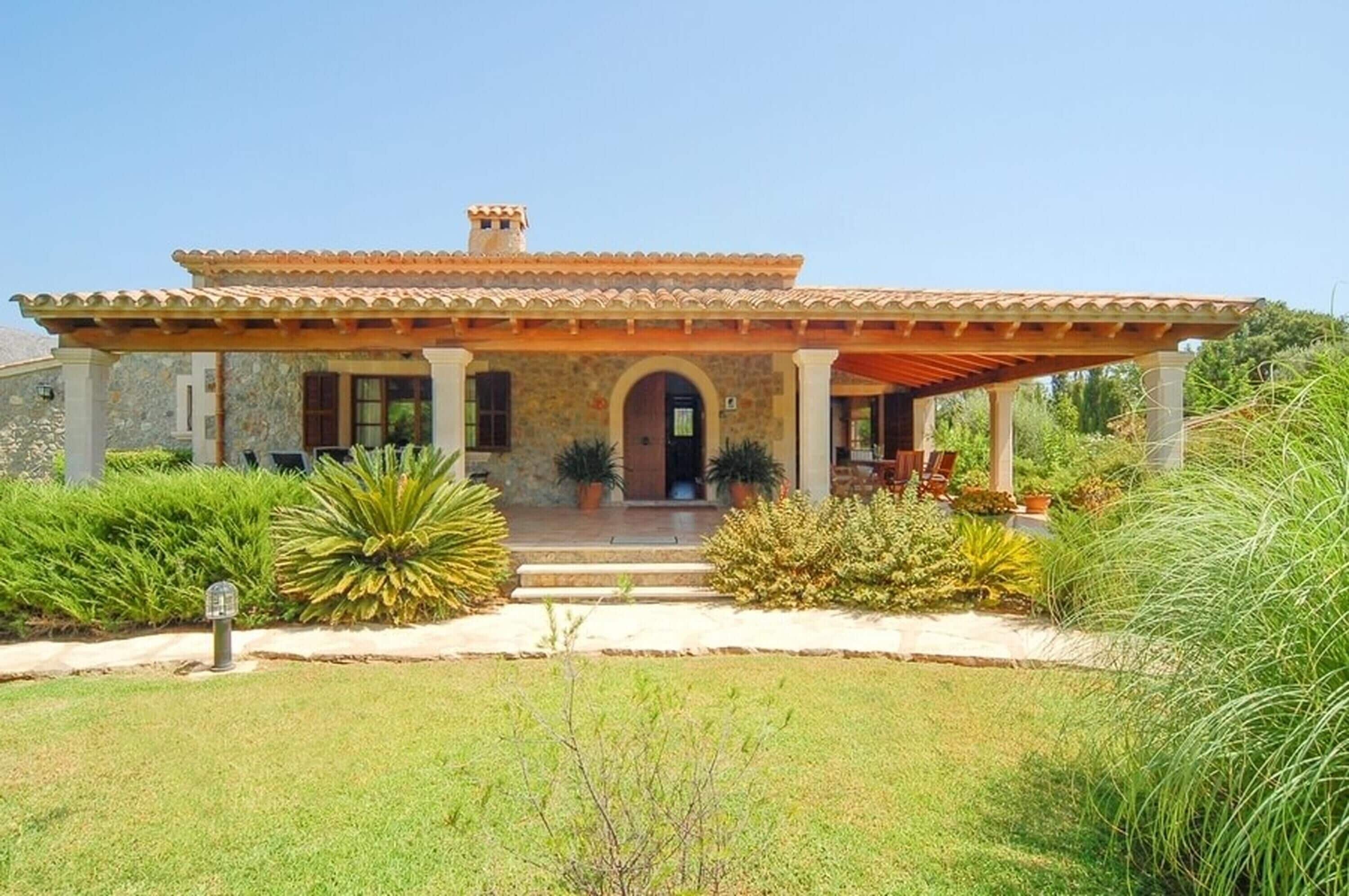 A house with a stone facade, a tiled roof, and a covered porch with potted plants.