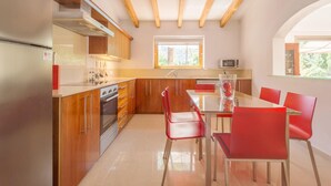Eine moderne Küche mit Holzschränken, einem Edelstahlkühlschrank und einem Essbereich mit roten Stühlen und einem Glastisch.