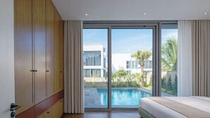 Een moderne slaapkamer met een groot bed, een kledingkast en uitzicht op een zwembad en gebouwen.