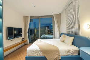 Ett modernt hotellrum med en stor säng, en platt-TV, en glasdörr som leder ut till en balkong och utsikt över staden.
