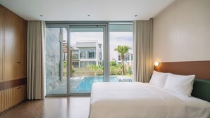 Een hotelkamer met een groot bed, een glazen schuifdeur naar een zwembad en uitzicht op een modern gebouw.