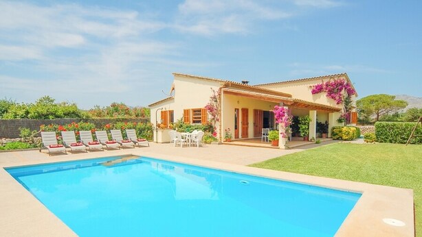 Una casa amb piscina, un pati amb seients i un jardí amb flors.