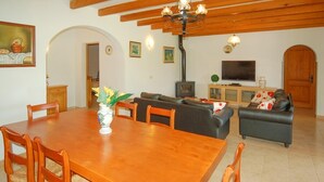 Zona de menjador amb taula i cadires de fusta, un sofà i una televisió al fons.