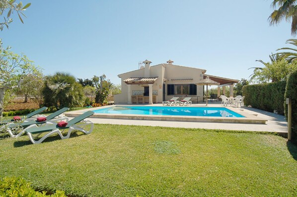 Une maison avec une piscine, des chaises longues et un patio couvert.