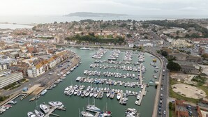 Un port de plaisance où sont amarrés de nombreux bateaux, entouré d’immeubles résidentiels et bordé par une route.