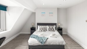 Une chambre moderne avec un grand lit, deux tables de chevet, une fenêtre avec des stores et un plafond en pente.
