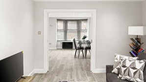 Un salon moderne doté d’un téléviseur à écran plat, d’un canapé gris agrémenté de coussins à motifs et d’un coin repas avec une table et des chaises.