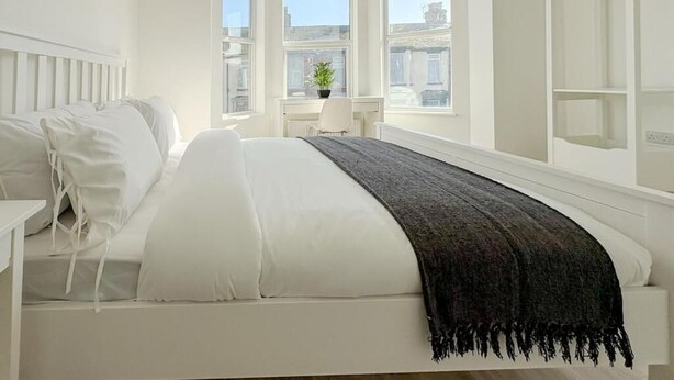 A bedroom with a bed, a bedside table, a window, and a view of the city. - Nelson Road - 3 Bed Terrace in Yarmouth (Great Yarmouth)