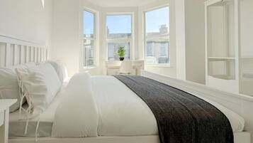 A bedroom with a bed, a bedside table, a window, and a view of the city.
