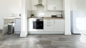 A modern kitchen with white cabinetry, a stainless steel range hood, a built-in oven, and a refrigerator. - Nelson Road - 3 Bed Terrace in Yarmouth (Great Yarmouth)