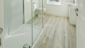A modern bathroom with a glass shower enclosure, a toilet, and a window providing natural light. - Nelson Road - 3 Bed Terrace in Yarmouth (Great Yarmouth)
