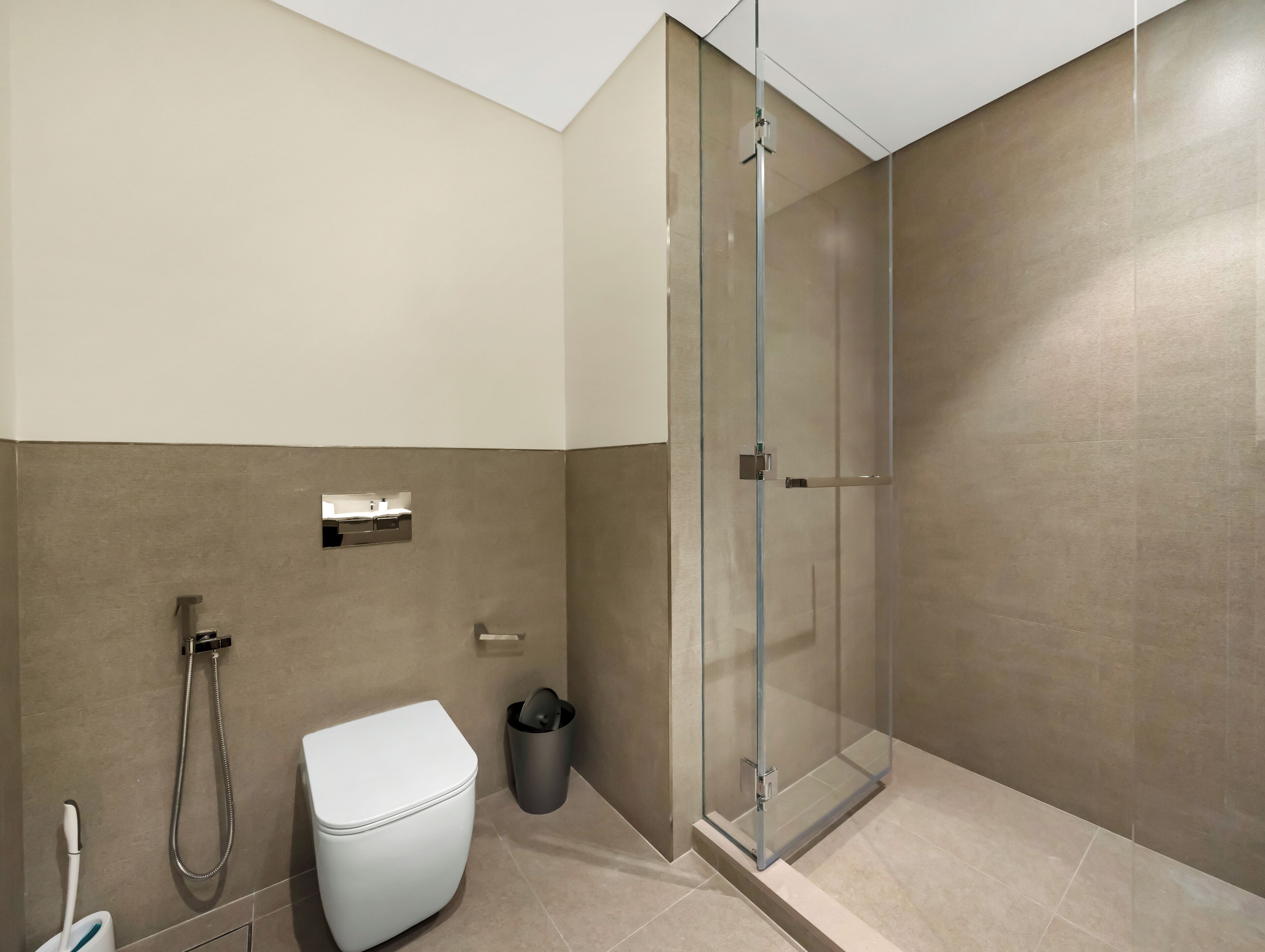 A modern bathroom with a glass-enclosed shower, a toilet, and a trash bin.