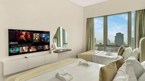 Une chambre d’hôtel avec deux lits, un téléviseur fixé au mur affichant l’interface Netflix, une fenêtre donnant sur la ville et un luminaire au plafond.