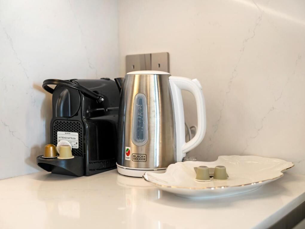 Una cafetera, un hervidor y un plato con tazas sobre una encimera.