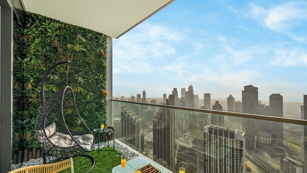 Un balcon offrant une vue sur les gratte-ciel de la ville, un fauteuil suspendu, une table avec des boissons et un mur végétal.