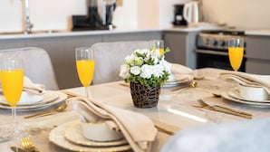 Une table à manger dressée avec des assiettes, des verres et des couverts, un vase rempli de fleurs et, au fond, une machine à café.