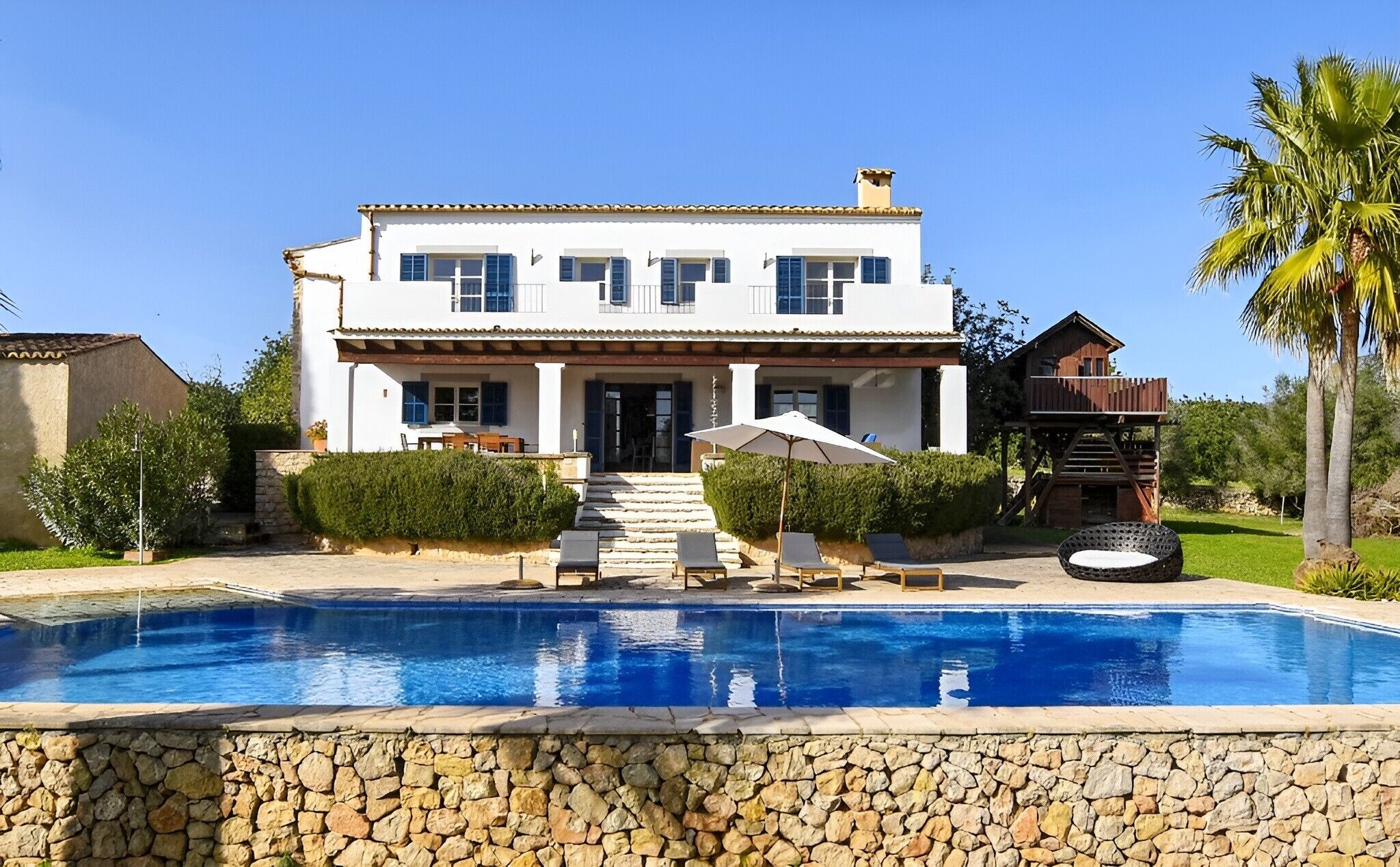 Una casa de dos pisos con piscina, un patio cubierto y una terraza de madera.