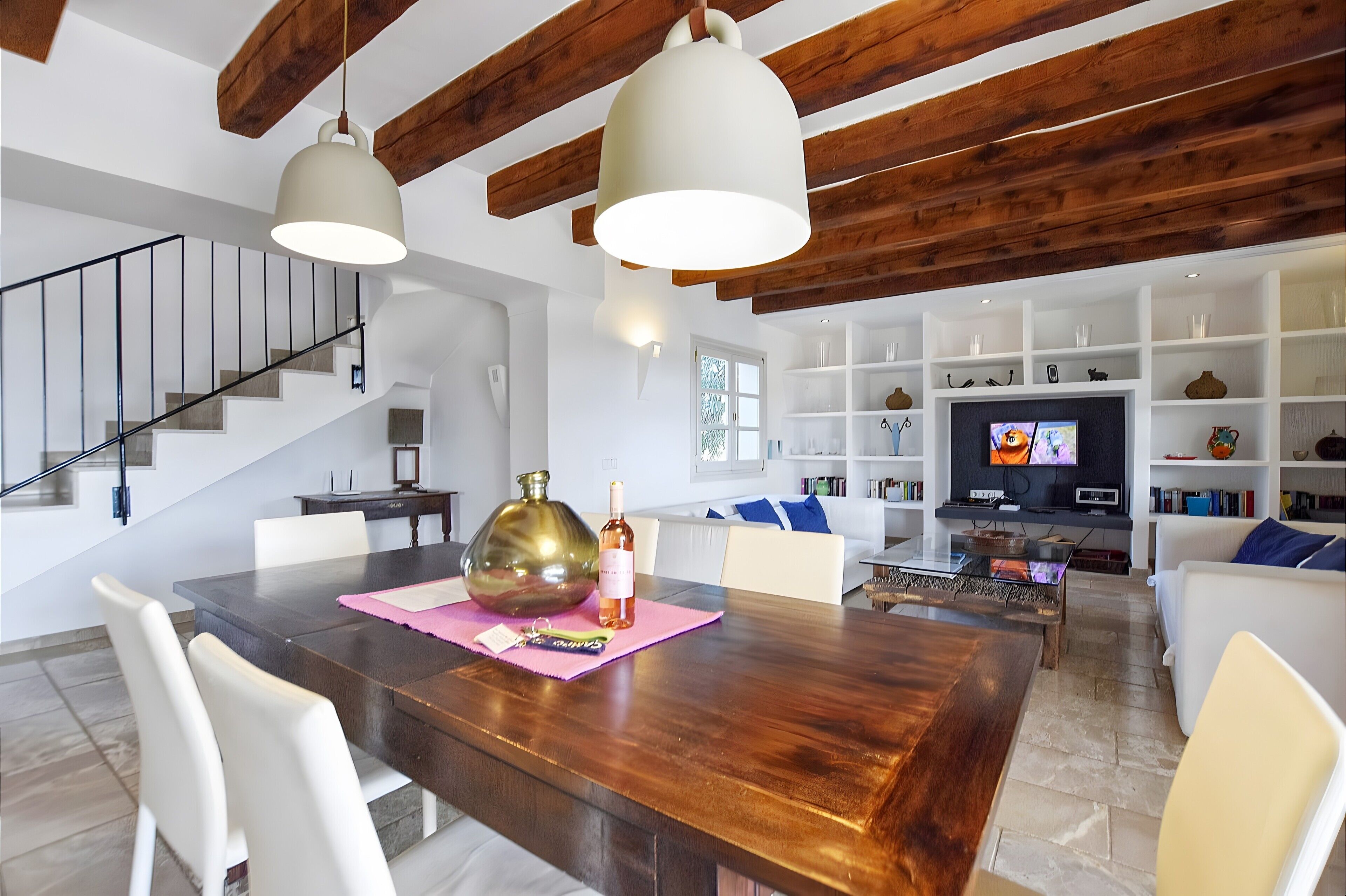 A modern living room with a wooden dining table, white sofas, a TV, and built-in shelves.
