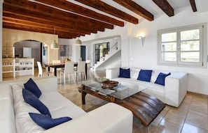 Een moderne woonkamer met een witte bank, een glazen salontafel en een trap naar een hoger niveau.