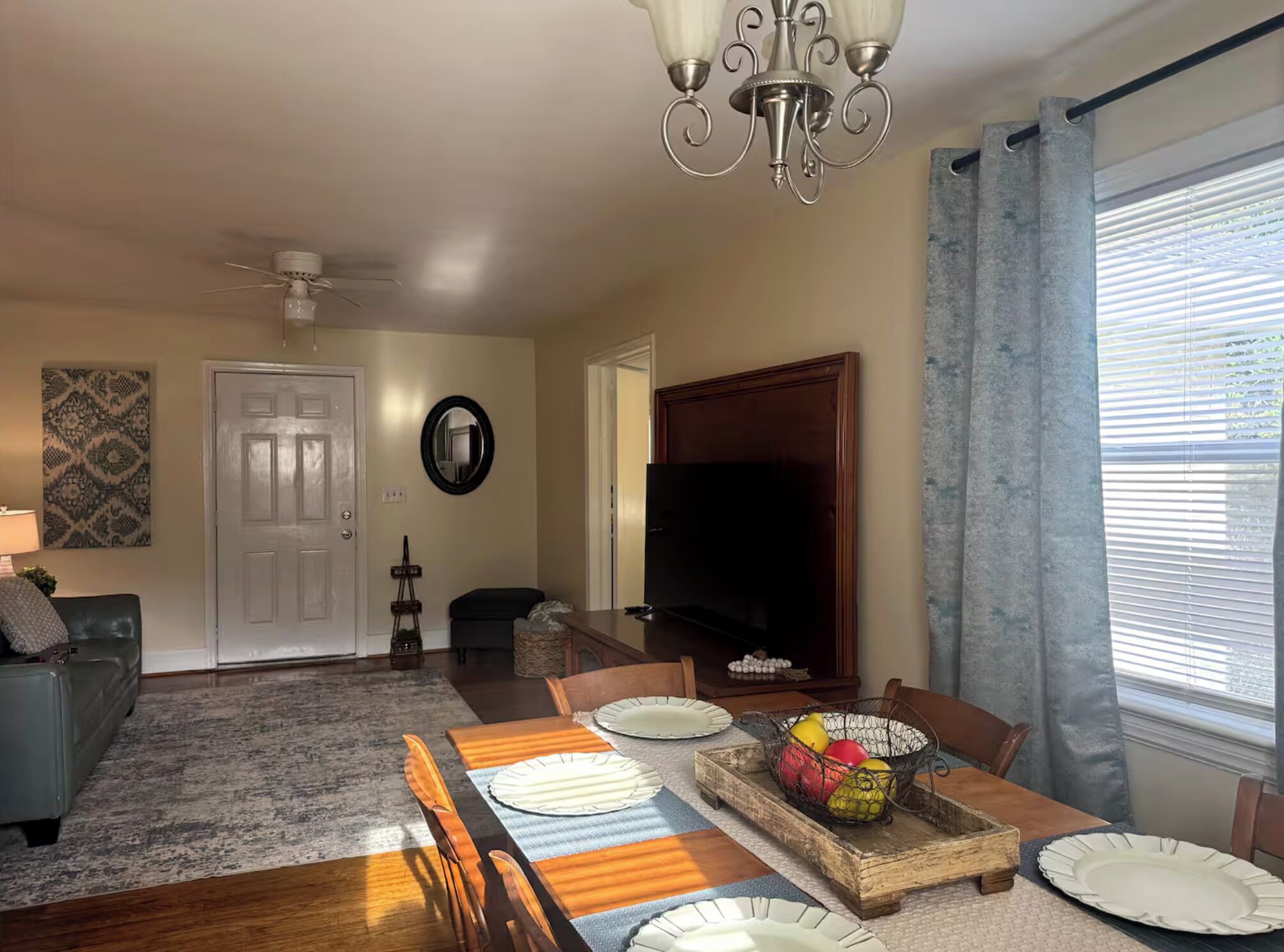 A dining area with a wooden table set for four, a chandelier, and a television in the background.